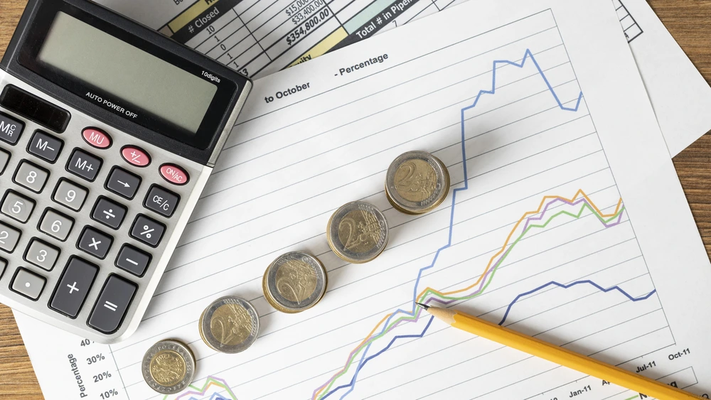 Calculator and stacked coins placed on printed financial charts with upward trend lines, showing cost calculation and risk evaluation context.