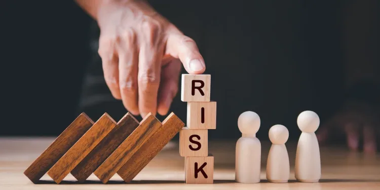 Hand placing a block labeled “Risk” in front of figures, illustrating risk assessment and decision-making in business systems.