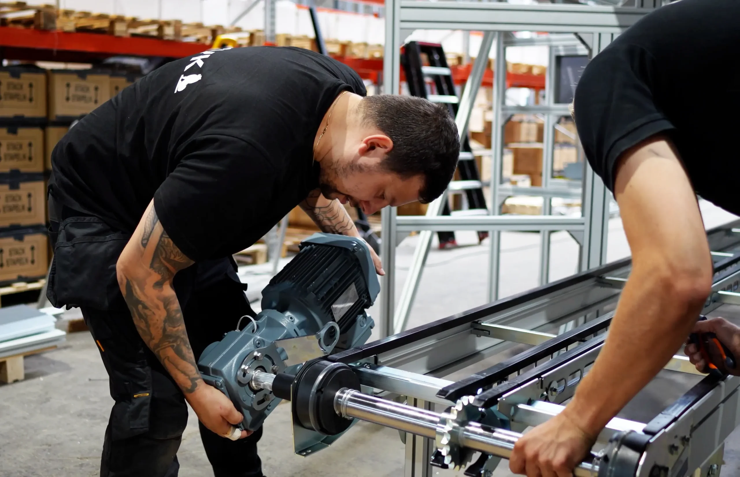 Technicians installing and adjusting mechanical components on an industrial production line inside a factory.